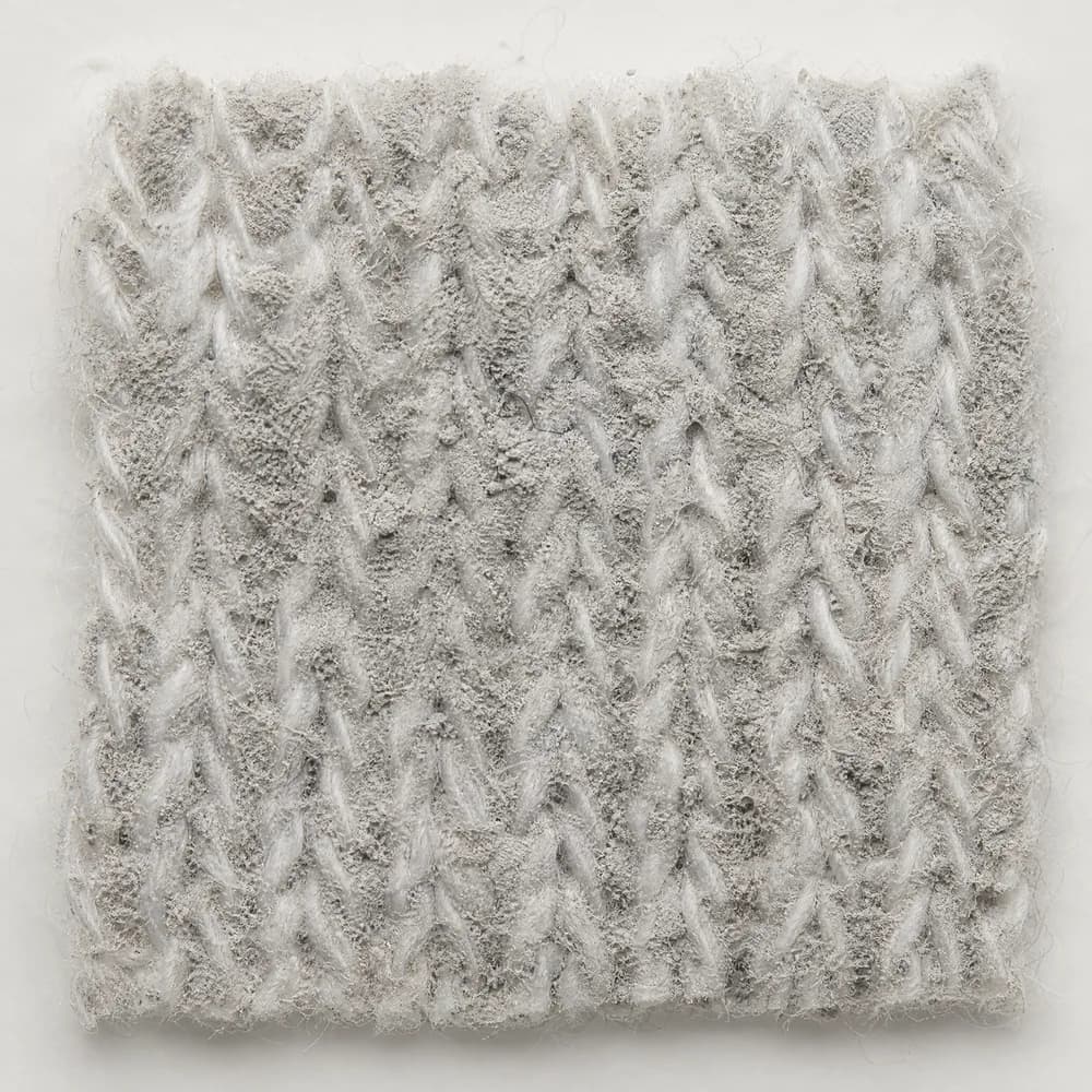 Extreme macro of white knitted cotton loops matted with a dull neutral-grey powdery film that has filled the spaces between them.