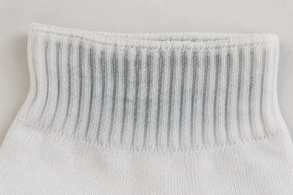 Close detail of the thick ribbed cuff of a white sock showing cool chalky dullness settled into the rib valleys.