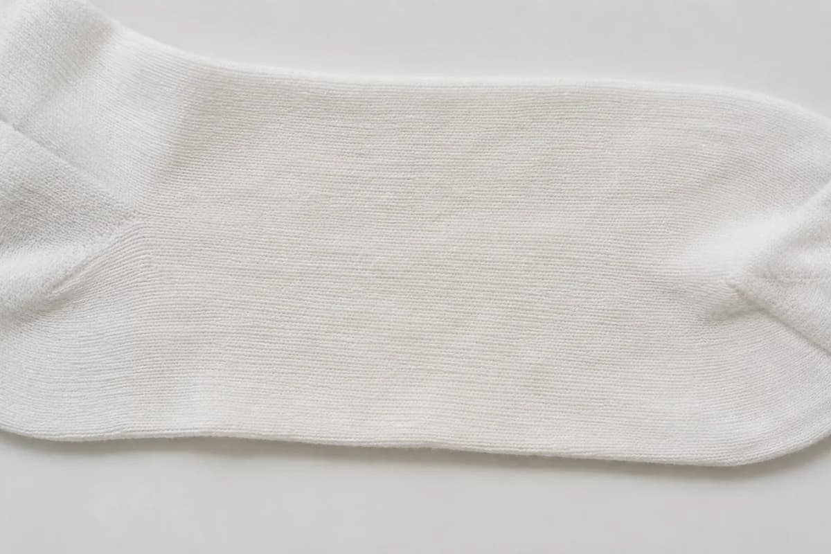 Close detail of the flat mid-leg panel of a white sock showing a faint even overall tint with no localised patch.