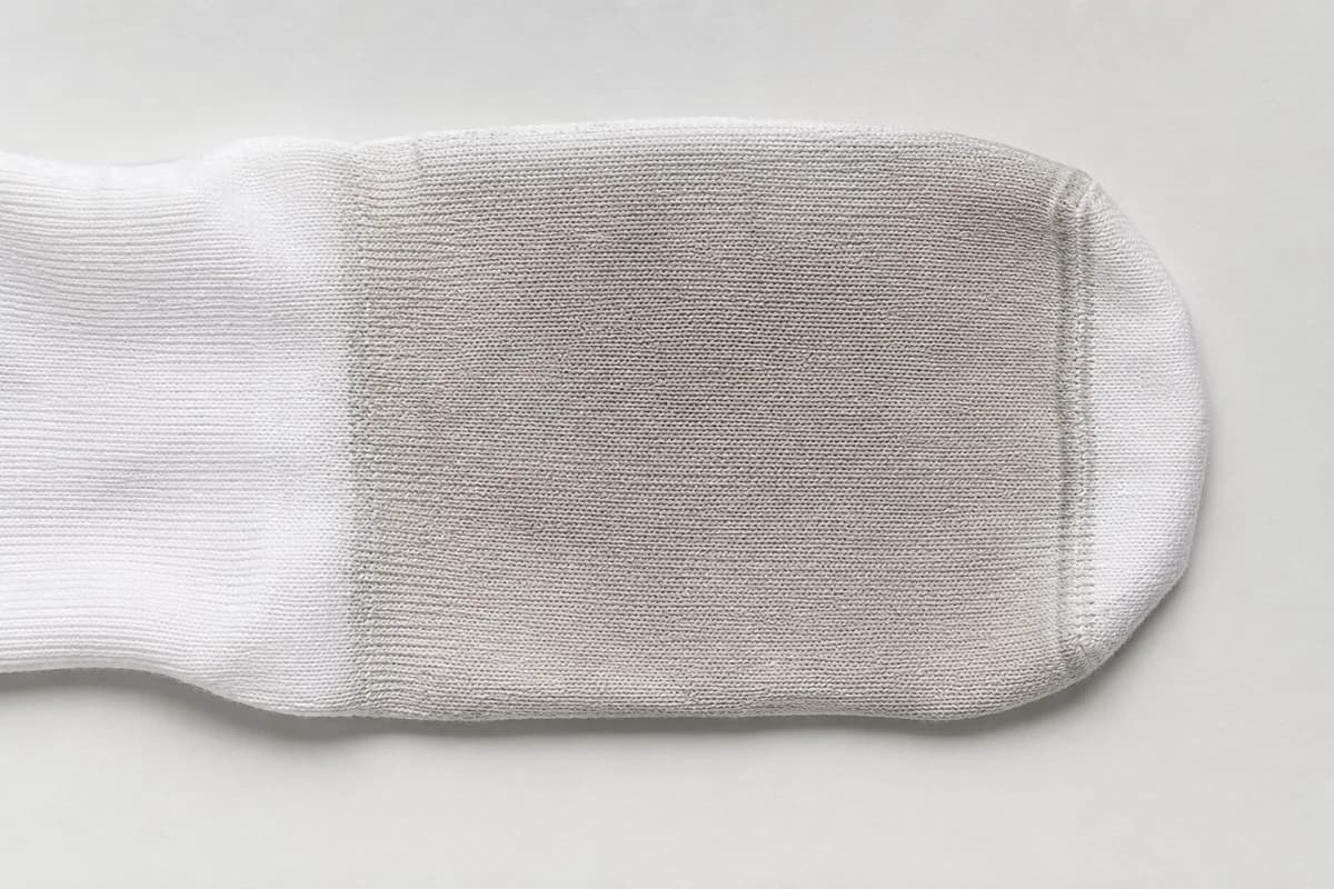 Close detail of the sole panel of a white sock showing an evenly shifted band of dense knit.