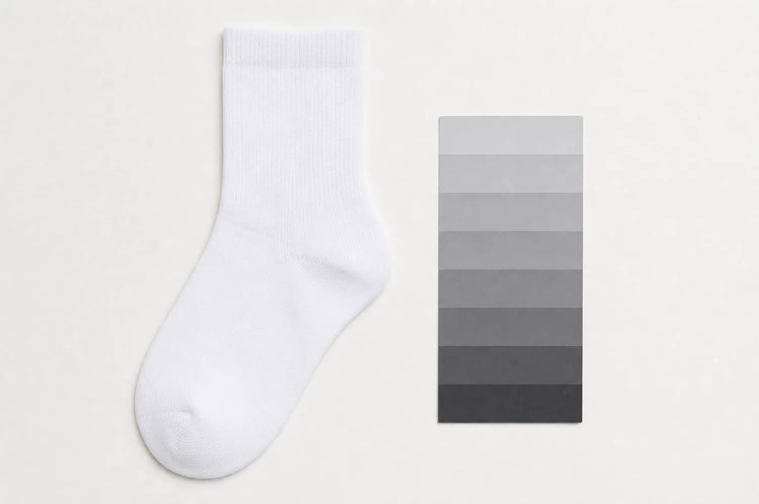 A white sock laid flat beside an unmarked grey step wedge card of neutral chips, for tonal reference.