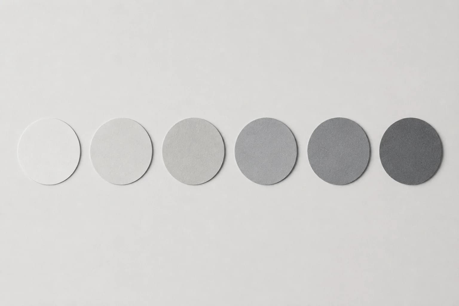 A row of plain unmarked neutral grey paper chips stepping from near-white to mid-grey, laid flat and evenly spaced.