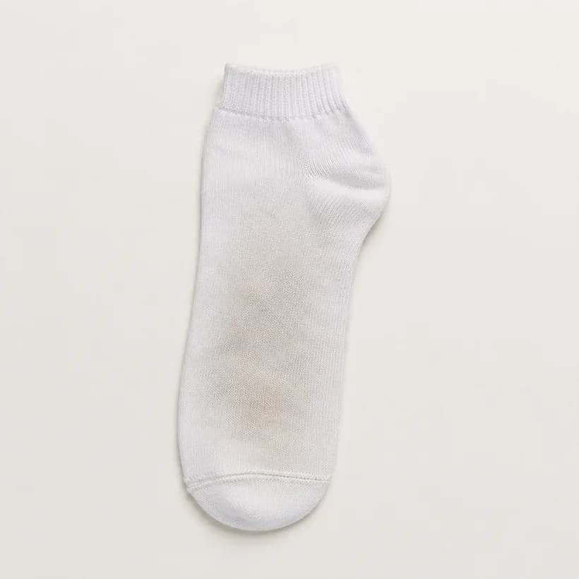A small white child's ankle sock laid flat with a soft-edged greyed band across the sole.