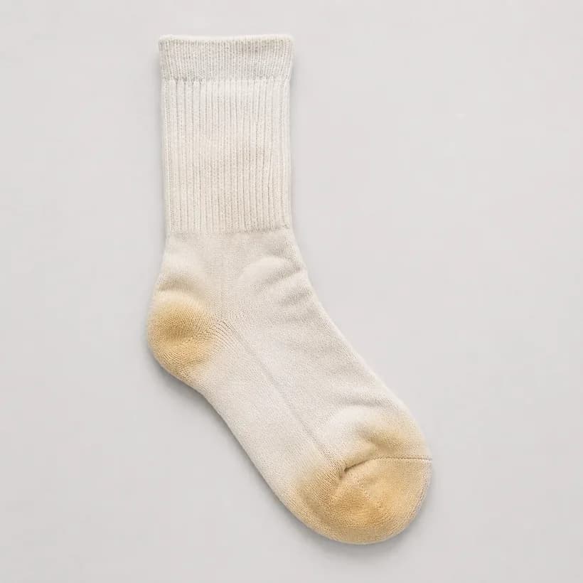 A thick white boot sock laid flat with warm yellowing at the heel pad and under the toes.